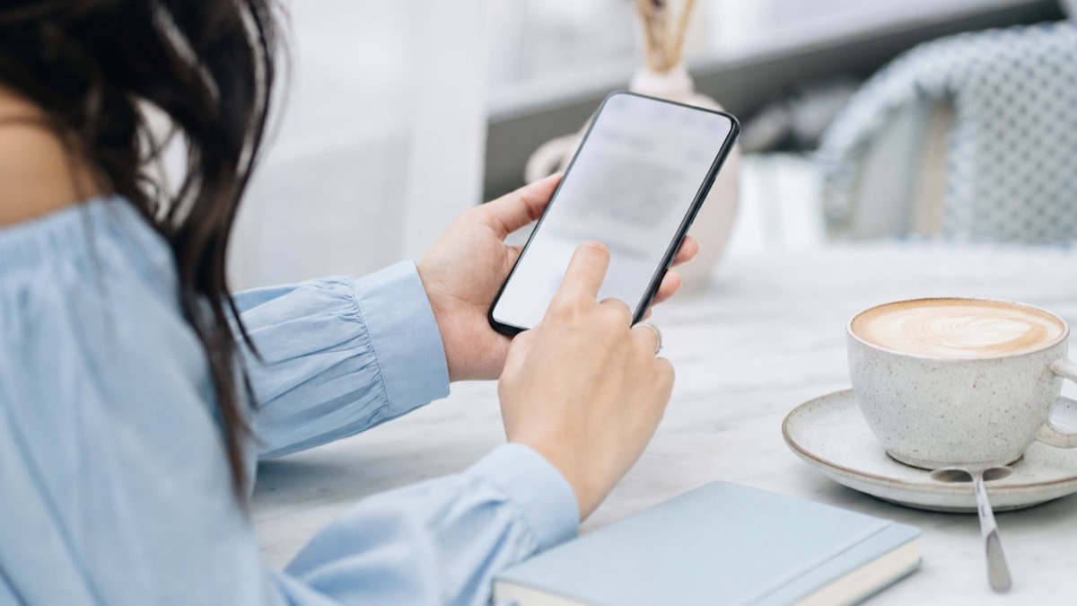 A customer at a cafe table tapping a reply on her phone next to a latte